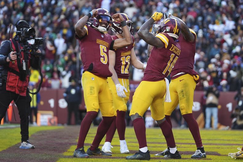 El receptor abierto de los Commanders de Washington, Olamide Zaccheaus (14), celebra su touchdown con el quarterback, Jayden Daniels (5), y otros durante la segunda mitad de un partido contra los Eagles de Filadelfia, el domingo 22 de diciembre de 2024, en Landover, Maryland (AP Foto/Stephanie Scarbrough)