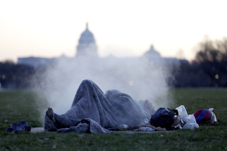 ARCHIVO - El Capitolio de Estados Unidos sirve de fondo a un hombre sin hogar que descansa en una chimenea de vapor en el National Mall, el 18 de diciembre de 2019, en el Capitolio de Washington. (AP Foto/Julio Cortez, archivo)