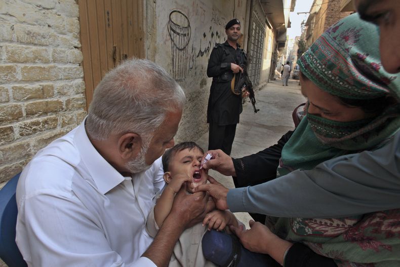 Un policía monta guardia mientras una trabajadora de salud, a la derecha, administra una vacuna de la polio a un niño en un vecindario de Peshawar, Pakistán, el lunes 28 de octubre de 2024. (AP Foto/Mohammad Sajjad)