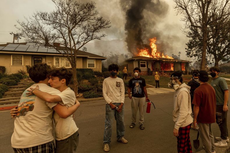 ARCHIVO - Vecinos se abrazan en el exterior de una propiedad en llamas mientras el incendio Eaton arrasa la zona el miércoles 8 de enero de 2025 en Altadena, California. (AP foto/Ethan Swope, archivo)