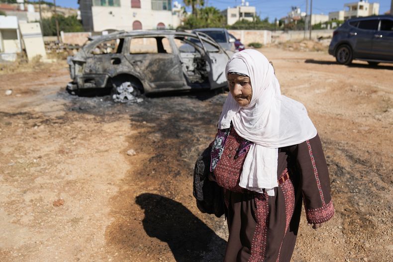 Una mujer camina frente a un vehículo que fue quemado por colonos israelíes como parte de un ataque que dejó tres palestinos muertos y varios vehículos y viviendas dañadas, de acuerdo con residentes del poblado de Kafr Malik, el jueves 26 de junio de 2025, en Cisjordania. (AP Foto/Nasser Nasser, Archivo)