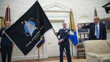 El general John Jay Raymond, comandante del Comando Espacial Estadounidense (izq) y el sargento Roger Towberman (der) sostienen la bandera al lado del presidente Donald Trump durante la presentación de la bandera del Comando Espacial en la Oficina Oval en la Casa Blanca en Washington el 15 de mayo del 2020. (AP foto/Alex Brandon)