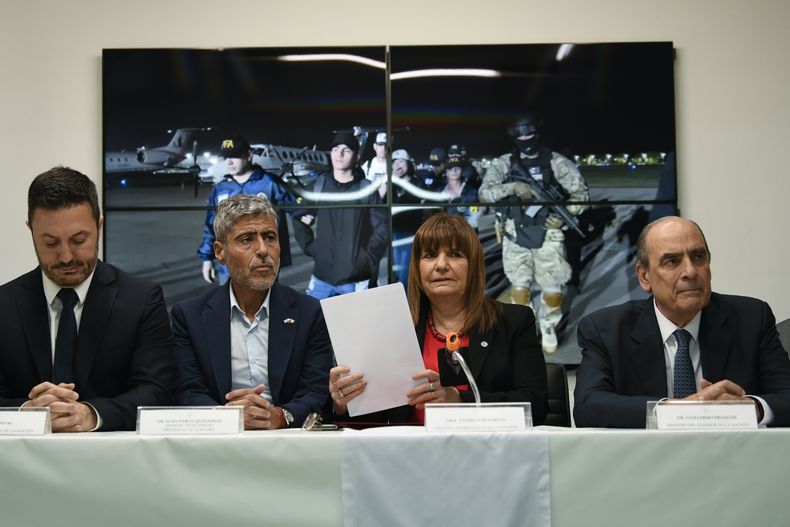 La ministra de Seguridad, Patricia Bullrich, segunda desde la derecha, el ministro de Defensa, Luis Petri, a la izquierda, el ministro de Seguridad de Córdoba, Juan Pablo Quinteros, segundo desde la izquierda, y el ministro del Interior, Guillermo Francos, a la derecha, dan una conferencia de prensa sobre la expulsión de la familia del prófugo narco ecuatoriano José Adolfo Fito Macías Villamar, mostrado en video detrás de ellos, en Buenos Aires, Argentina, el viernes 19 de enero de 2024. El líder de Los Choneros desapareció de una prisión de Guayaquil unas semanas antes. (Foto AP/Gustavo Garello)
