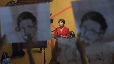 americateve | Manifestantes sostienen en lo alto imagenes de Edward Snowden al momento en que irrumpen en una ceremonia en la que la presidenta Dilma Rousseff, al fondo, pronunciaba un discurso de fin de a&ntilde;o ante trabajadores y personas sin casa en Sao Paulo, Br