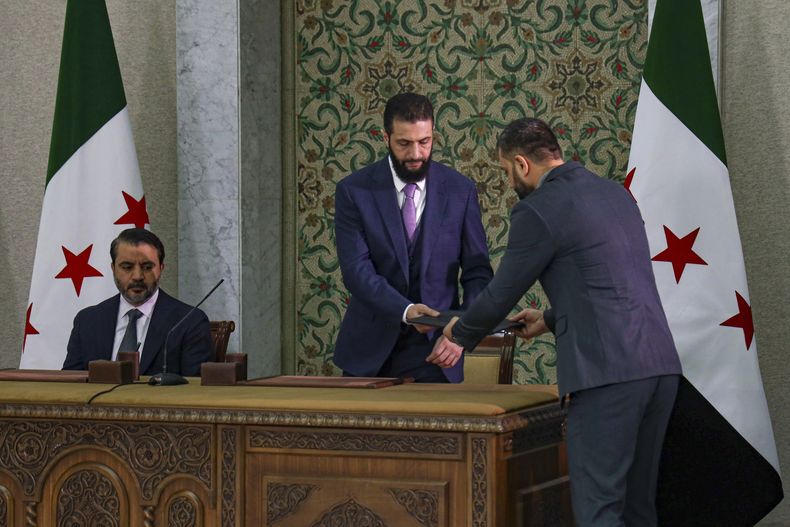 El presidente interino de Siria, Ahmad Al-Sharaa, centro, se prepara para firmar una Constitución temporal para el país en Damasco, Siria, el jueves 13 de marzo de 2025. A la izquierda, el ministro de Exteriores Asaad Hassan al-Shiban. (AP Foto/Omar Albam)
