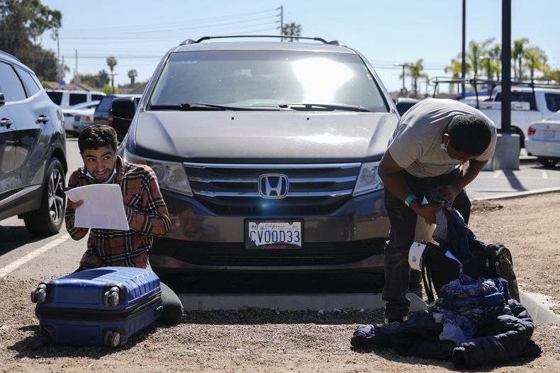 Dos inmigrantes revisan su equipaje en un estacionamiento tras ser detenidos por las autoridades estadounidenses y procesados para ver si se les concede asilo, el martes 7 de mayo de 2024, en San Diego. (AP Foto/Ryan Sun)