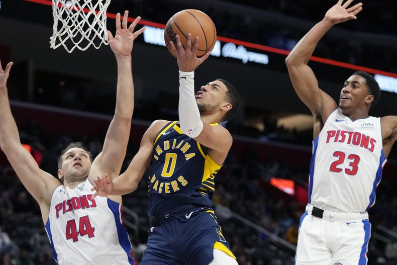 Tyrese Haliburton (0), de los Pacers de Indiana, intenta una bandeja ante la presión defensiva de Bojan Bogdanovic (44) y Jaden Ivey (23) durante la primera mitad del juego de baloncesto de la NBA, el lunes 11 de diciembre de 2023, en Detroit. (AP Foto/Carlos Osorio)