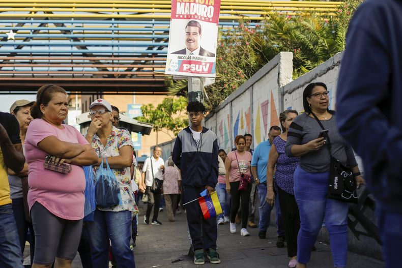 Los votantes hacen fila en un colegio electoral donde cuelga un cartel de campaña del presidente Nicolás Maduro durante las elecciones presidenciales en Caracas, Venezuela, el domingo 28 de julio de 2024. (AP Foto/Cristian Hernández)
