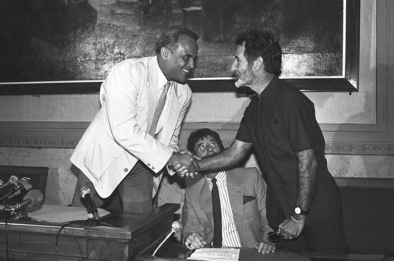 El escritor sudafricano Breyten Breytenbach, a la derecha, y el actor y cantante estadounidense Harry Belafonte se saludan durante una conferencia de prensa, el 18 de junio de 1986, en París. (AP Foto, Archivo)