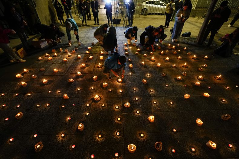 Varias personas encienden velas durante una vigilia frente a la sede de los carabineros en honor de tres policías asesinados en el sur de Chile, el sábado 27 de abril de 2024, en Santiago. (AP Foto/Esteban Félix)