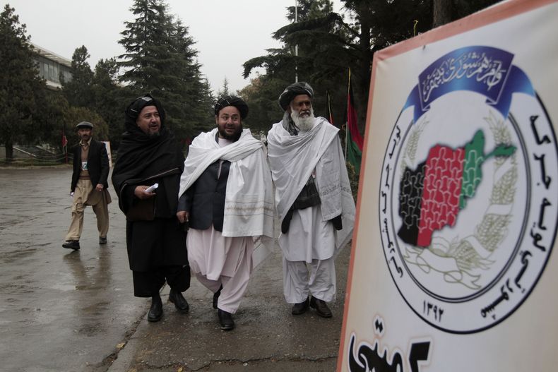 Delegados afganos pasan junto a un cartel de Loya Jirga, una asamblea conformada por miles de personalidades prominentes de todo el pa&iacute;s, en el tercer d&iacute;a de reuniones en Kabul, Afganist&aacute;n, el s&aacute;bado 23 de noviembre de 2013. El