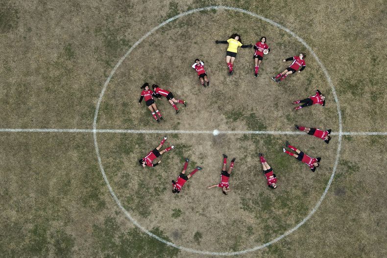 Candelaria Cabrera, arriba, sostiene un balón y posa con sus compañeras del Huracán de Chabas femenino en el campo antes del juego ante el Alumni in Arequito en Argentina, el lunes 19 de junio del 2023. (AP Foto/Natacha Pisarenko)