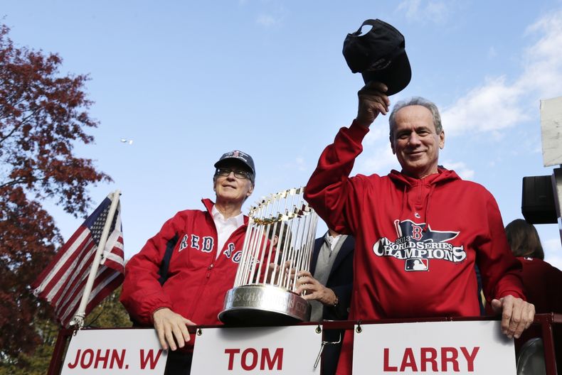 ARCHIVO - El presidente de los Medias Rojas de Boston Larry Lucchino (derecha) saluda a los fanáticos junto al dueño John Henry durante el desfile de celebración por la consagración en la Serie Mundial de 2013, el 2 de noviembre de 2013, en Boston. Lucchino ha fallecido. Tenía 78 años. (AP Foto/Charles Krupa)