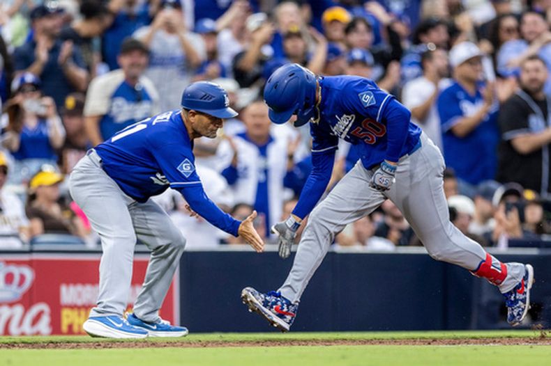 Mookie Betts (50), derecha, de los Dodgers de Los Ángeles, choca manos con el coach de tercera base, Dino Ebel, después de batear un cuadrangular de tres carreras en la sexta entrada del juego de béisbol de Grandes Ligas ante los Padres de San Diego, el sábado 27 de junio de 2026, en San Diego. (AP Foto/Tony Ding)