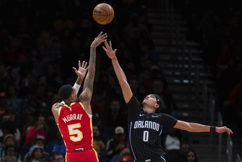 El base de los Hawks de Atlanta Dejounte Murray lanza el balón para triple sobre Anthony Black del Magic de Orlando en el encuentro de la NBA del domingo 25 de febrero del 2024. (AP Foto/Hakim Wright Sr.)