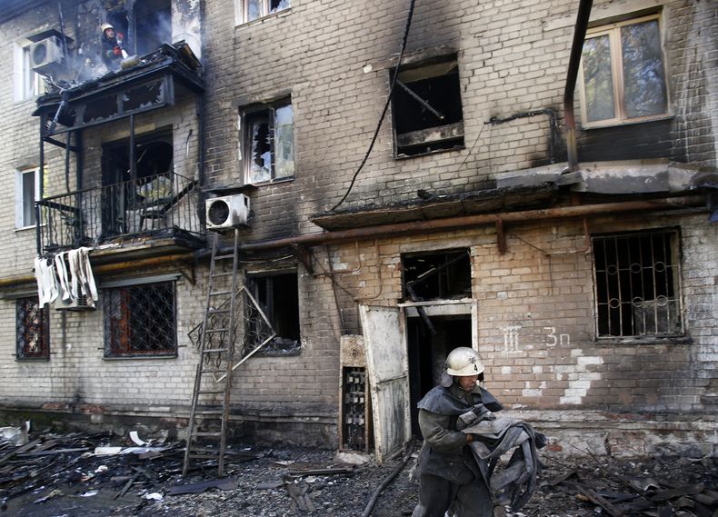 Un bombero lleva una manguera hasta un edificio da&ntilde;ado por cohetes en la localidad de Donetsk, en el este de Ucrania, el 17 de septiembre de 2014. Dos personas murieron y tres resultaron heridas el mi&eacute;rcoles en la ciudad de Donetsk, en el es