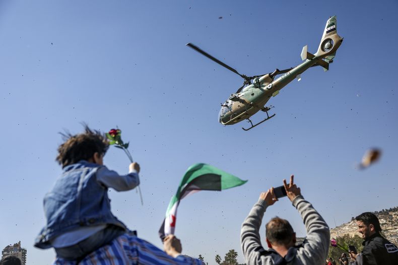 Un helicóptero del ejército sirio lanza flores y confeti sobre un grupo de manifestantes que conmemoran el aniversario 14 del inicio del levantamiento contra el régimen de Bashar Assad en marzo de 2011, en la plaza de los Omeyas, Damasco, Siria, sábado 15 de marzo de 2025. (AP foto/Ghaith Alsayed)