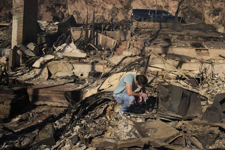 Luke Dexter se agacha mientras revisa los restos de la casa de la playa de su padre, arrasada por el incendio Palisades, el 10 de enero de 2025, en Malibú, California. (AP Foto/John Locher)