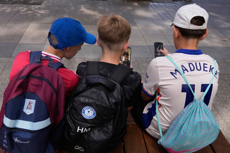ARCHIVO - Tres niños utilizan sus celulares sentados en el exterior de una escuela en Sydney, el 8 de diciembre de 2025. (AP Foto/Rick Rycroft, archivo)