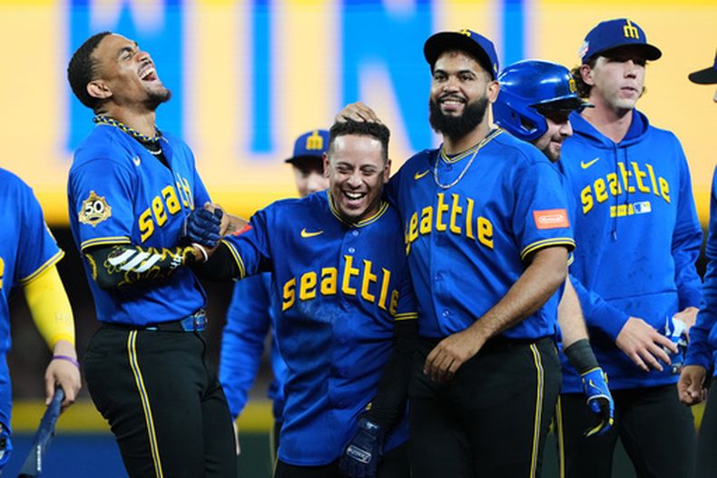 El venezolano Leo Rivas, de los Marineros de Seattle, festeja con sus compañeros, los dominicanos Julio Rodríguez (izquierda) y Seranthony Domínguez (3ro de izquierda a derecha) luego de pegar un sencillo productor en la décima entrada ante los Cachorros de Chicago, el viernes 21 de agosto de 2026 (AP Foto/Lindsey Wasson)