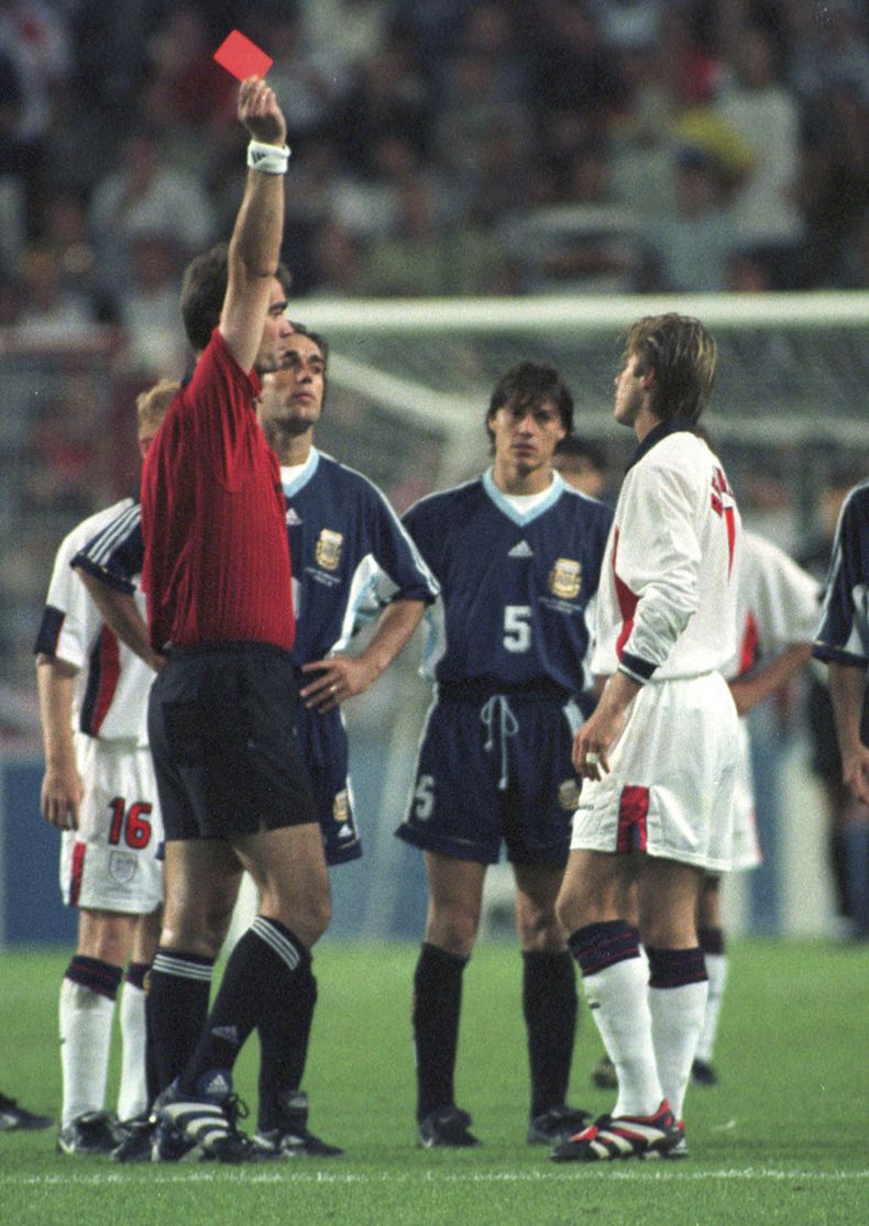 ARCHIVO - El jugador inglés David Beckham recibe una tarjeta roja del árbitro danés Kim Milton Nielsen por patear al jugador argentino Diego Simeone, durante el partido de fútbol de segunda ronda de la Copa Mundial entre Inglaterra contra Argentina, en Saint Etienne, Francia, el 30 de junio de 1998. Inglaterra perdió en penales después de que terminó el partido 2 -2. La serie documental de Netflix, Beckham, que se estrena el 4 de octubre de 2023, explora la crianza de Beckham, sus triunfos y tropiezos. (Foto AP/Denis Doyle, archivo)