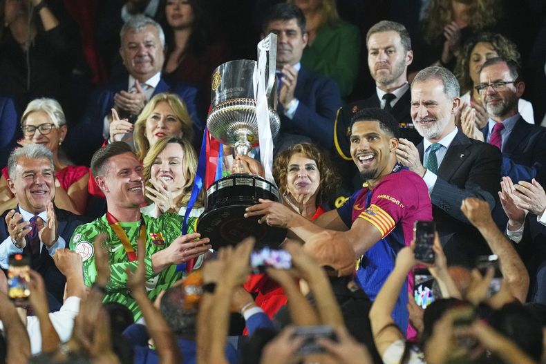 Ronald Araujo y el arquero Marc-André ter Stegen del Barcelona levantan el trofeo después de ganar la final de la Copa del Rey de España ante el Real Madrid, el domingo 27 de abril de 2025, en Sevilla. (Foto AP/José Bretón)
