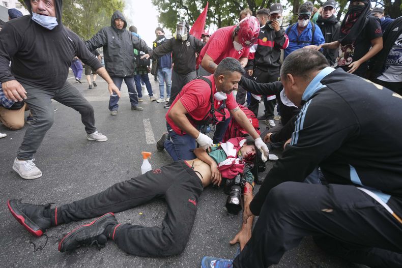 Médicos atienden a un fotógrafo herido durante los enfrentamientos que estallaron cuando los aficionados al fútbol se unieron a los jubilados para exigir pensiones más altas y oponerse a las medidas de austeridad implementadas por el gobierno de Javier Milei en Buenos Aires, Argentina, el miércoles 12 de marzo de 2025. (Foto AP/Rodrigo Abd)