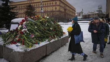 Gente coloca flores y presenta sus respetos a Alexei Navalny en un momento, una roca de las islas Solovetsky, donde se estableció el primer campamento del sistema de prisiones políticas de Gulags, con el edificio histórico del Servicio Federal de Seguridad (FSB, el sucesor del KGB soviético) al fondo, en Moscú, Rusia, el sábado 17 de febrero de 2024. (AP Foto/Alexander Zemlianichenko)