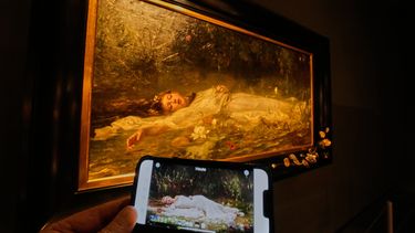 En el celular, el video de la canción The Fate of Ophelia de Taylor Swift, y al fondo, el cuadro en que se inspiró, obra de Friedrich Heyser, en un museo en Wiesbaden, Alemania, el 16 de octubre del 2025. (AP foto/Michael Probst)