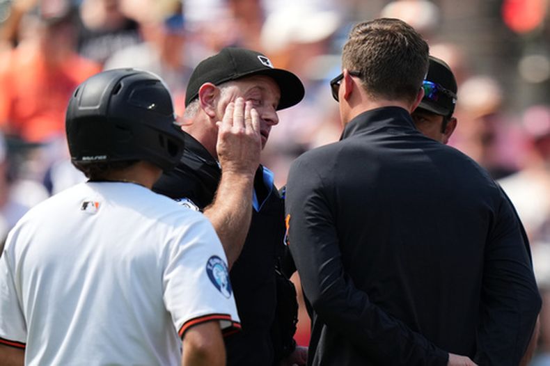 El umpire de home Chris Guccione (el segundo de la izquierda) conversa con un preparador físico y otros oficiales tras recibir el impacto de un foul tip en la careta durante la segunda entrada de un partido de béisbol entre los Orioles de Baltimore y los Guardianes de Cleveland, el lunes 7 de septiembre de 2026, en Baltimore. (Foto AP/Stephanie Scarbrough)