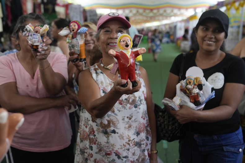 Varias mujeres enseñan sus figuras en miniatura del dios pagano andino Ekeko, de la abundancia, la fertilidad y la felicidad, en una feria indígena en Lima, Perú, el viernes 24 de enero de 2025. (AP Foto/Martín Mejía)