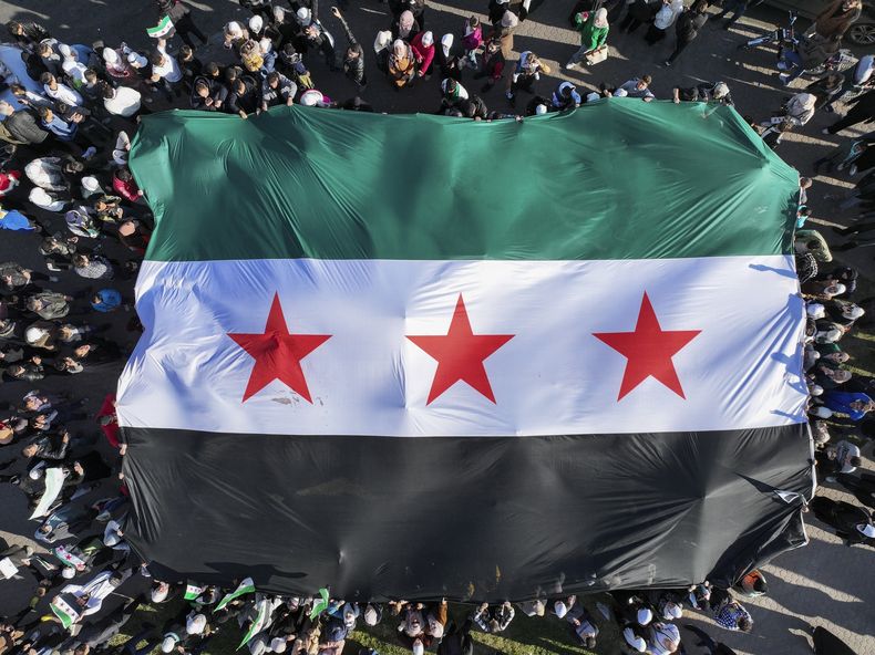 Sirios extienden una enorme bandera revolucionaria siria durante una manifestación de celebración tras las primeras plegarias de viernes desde la caída del expresidente Bashar Assad, en la plaza central de Damasco, Siria, el viernes 13 de diciembre de 2024. (AP Foto/Ghaith Alsayed)