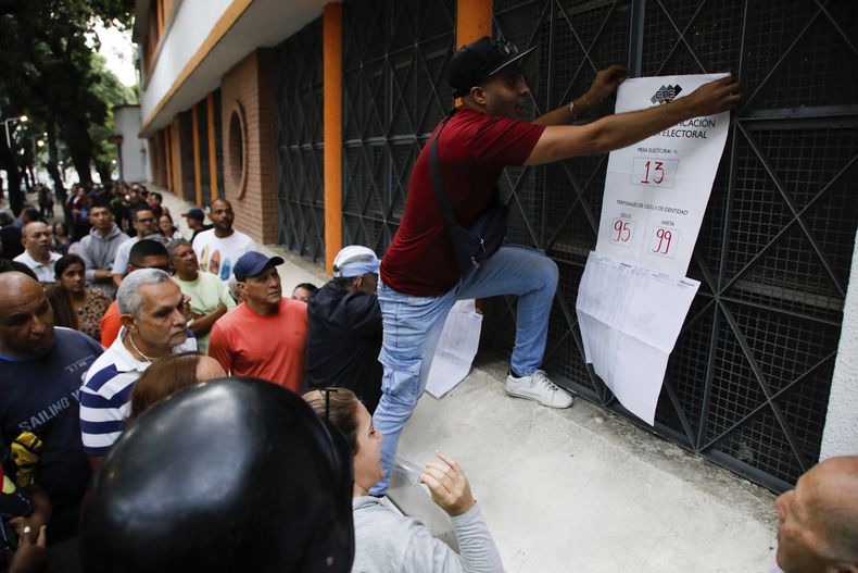 Un funcionario electoral publica información sobre los colegios electorales mientras se retrasa la apertura de las urnas para las elecciones presidenciales en la Escuela Andrés Bello, el principal centro de votación en Caracas, Venezuela, el domingo 28 de julio de 2024. (AP Foto/Cristian Hernández)