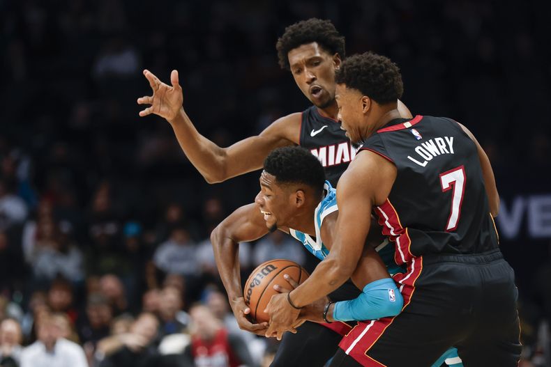 Brandon Miller, centro, de los Hornets de Charlotte, trata de mantener la posesión del balón entre dos jugadores del Heat de Miami, Josh Richardson y Kyle Lowry (7), durante la primera mitad del juego de baloncesto de la NBA del lunes 11 de diciembre de 2023, en Charlotte, Carolina del Norte. (AP Foto/Nell Redmond)