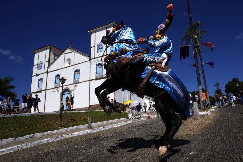 Un jinete, con una máscara de toro en la cabeza, participa en la Fiesta de las celebraciones Divinas como parte del festival de las Cavalhadas, el sábado 18 de mayo de 2024, en Pirenópolis, estado de Goiás, Brasil. Al fondo se encuentra la parroquia de Nuestra Señora del Rosario. La tradición de las Cavalhadas fue traída a Brasil en el siglo XIX por un sacerdote portugués para celebrar al Espíritu Santo y conmemorar la victoria de los caballeros ibéricos cristianos sobre los moros. (AP Foto/Eraldo Peres)