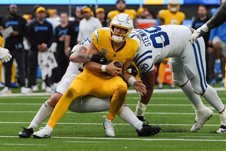 El quarterback Justin Herbert (10) de los Chargers de Los Ángeles es tacleado por el ala defensiva Laiatu Latu (97) y el tackle defensivo Grover Stewart (90) de los Colts de Indianápolis durante la segunda mitad de un juego de fútbol americano de la NFL el domingo 19 de octubre de 2025, en Inglewood, California. (AP Photo/Gregory Bull)