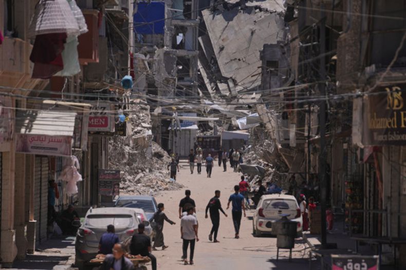 Varios palestinos caminan por una calle rodeada de edificios destruidos por ataques del ejército israelí durante la guerra entre Israel y Hamás en Jan Yunis, en el sur de la Franja de Gaza, el viernes 29 de mayo de 2026. (AP Foto/Abdel Kareem Hana)