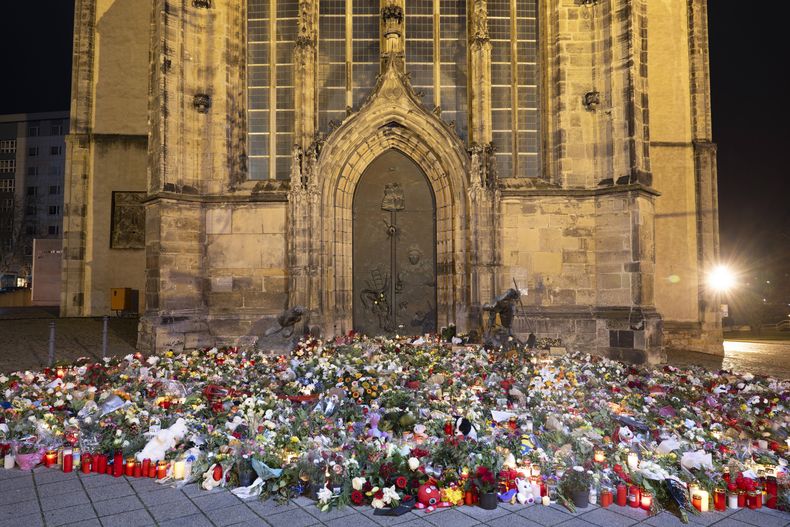 Velas, flores y guirnaldas frente a la entrada de la iglesia de San Juan a primera hora del domingo 22 de diciembre de 2024, en Magdeburgo, Alemania, después de que un coche arrollara a una multitud en un mercado navideño el viernes 20 de diciembre. (Sebastian Kahnert/dpa via AP)