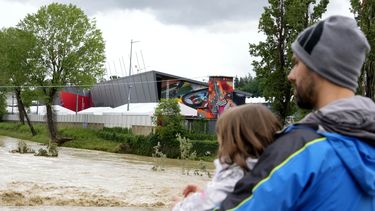Un hombre con un niño en brazos contempla la crecida del río Santerno, y en el fondo de ve el circuito Enzo e Dino Ferrari en Imola, Italia, 17 de mayo de 2023. Las inundaciones en la región han obligado a cancelar el Gran Premio de Fórmula Uno de la Emilia Romagna, que se debía correr en Imola el próximo fin de semana. (AP Foto/Luca Bruno)