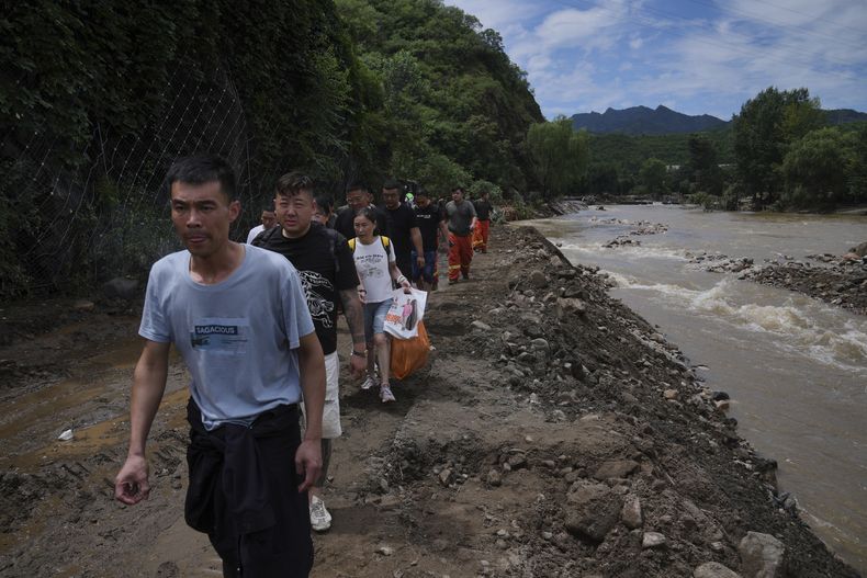 Gente caminando por una carretera que lleva al poblado de Langjiayu dañado por inundaciones, mientras evacúan la localidad tras fuertes lluvias en el distrito de Miyun, a las afueras de Beijing, el martes 29 de julio de 2025. (AP Foto/Andy Wong)
