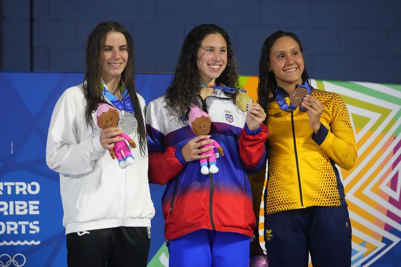 De izquierda a derecha, la mexicana Athena Meneses, la boricua Kristen Romano y la colombiana Jasmin Pistelli posan respectivamente con la plata, el oro y el bronce obtenidos en los 200 metros espalda de los Juegos Centroamericanos y del Caribe en San Salvador, el jueves 29 de junio de 2023 (AP Foto/Arnulfo Franco)