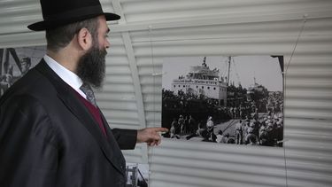 El rabino Arie Zeev Raskin mira una exhibición fotográfica en una réplica de las barracas de un campo de internamiento para refugiados judíos de Europa que trataban de llegar al territorio palestino tras la Segunda Guerra Mundial, en la ceremonia para conmemorar el 76to aniversario del cierre de una docena de dichos sitios, en el Campamento de la Guardia Nacional chipriota que albergó un hospital militar británico en Nicosia, el martes 18 de febrero de 2025. (AP Photo/Petros Karadjias)