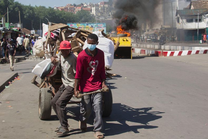 Vendedores callejeros tiran de un carro con sus mercancías mientras la policía choca con manifestantes durante una protesta pidiendo la renuncia del presidente, en Antananarivo, Madagascar, el jueves 9 de octubre de 2025. (AP Foto/Alexander Joe)