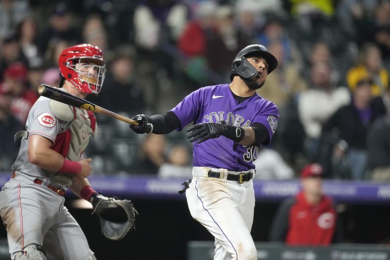 El venezolano Harold Castro, de los Rockies de Colorado, conecta un doble de dos anotaciones en la séptima entrada del partido contra los Rojos de Cincinnati en Denver, el lunes 15 de mayo de 2023. A la izquierda, el receptor de los Rojos, Tyler Stephenson. (AP Foto/David Zalubowski)