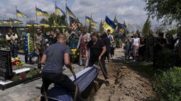 Un féretro con los restos de Roman Shadlovskyi es colocado en una fosa durante su nuevo entierro en Bucha, Ucrania, el martes 18 de julio de 2023. El veterano de las fuerzas armadas ucranianas, que fue enterrado en un principio en una fosa común como víctima no identificada tras ser asesinado el año pasad por tropas rusas, fue enterrado de nuevo el martes después de que una prueba de ADN confirmara su identidad. (AP Foto/Jae C. Hong)