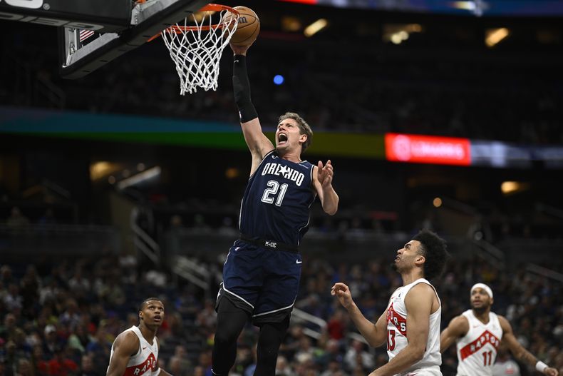 El pívot del Magic de Orlando Moritz Wagner (21) realiza una volcada mientras que el base de los Raptors de Toronto Ochai Agbaji (izquierda), el alero Jordan Nwora (segundo desde la derecha), y el escolta Bruce Brown (11) observan durante la primera mitad del juego de baloncesto de la NBA, el domingo 17 de marzo de 2024, en Orlando, Florida. (AP Foto/Phelan M. Ebenhack)