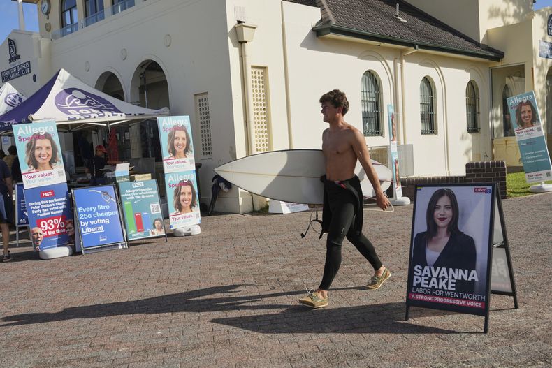 Un surfista pasa con su tabla por delante de un puesto de votación en Bondi Beach, Sydney, el 3 de mayo de 2025. (AP Foto/Mark Baker)