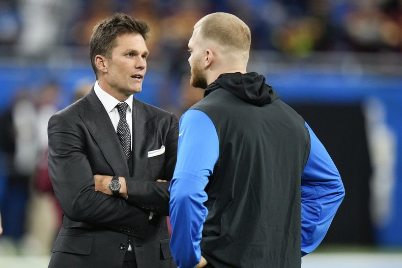 Tom Brady, izquierda, habla con Aidan Hutchinson, defensive end de los Lions de Detroit, previo a un partido de playoffs de la NFL en la ronda divisional en contra de los Commanders de Washington, el sábado 18 de enero de 2025, en Detroit. (AP Foto/Seth Wenig)