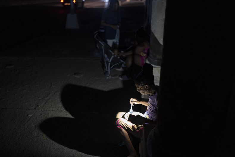 Una mujer ilumina su plato de alimentos valiéndose de la linterna de su teléfono en una calle durante un apagón general, el viernes 14 de marzo de 2025, en La Habana, Cuba. (AP Foto/Ramón Espinosa)