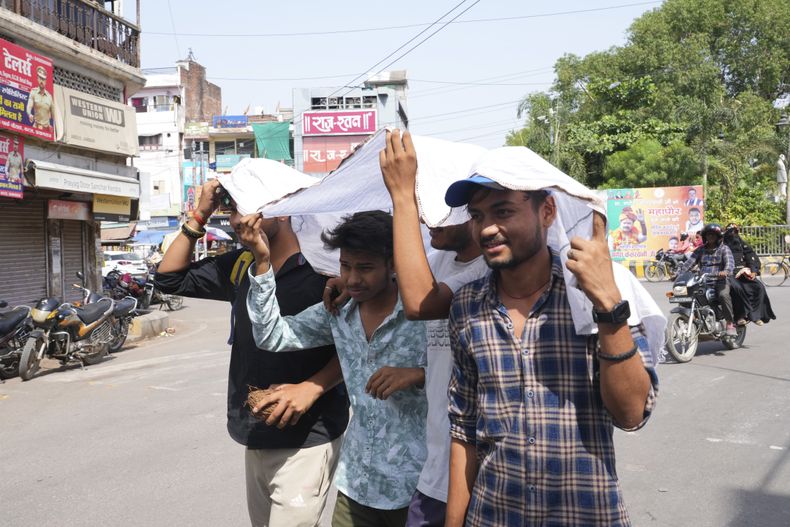 Jóvenes compartiendo un trozo de tela para protegerse del sol en un día caluroso de verano en Prayagraj, en el estado norteño de Uttar Pradesh, India, el domingo 21 de mayo de 2023. (AP Foto/Rajesh Kumar Singh)